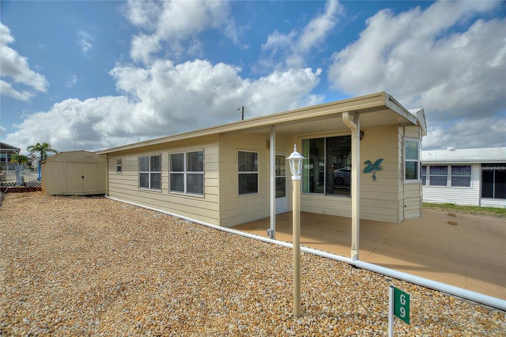 A light yellow mobile home with a covered porch and gravel yard under a cloudy sky — 251 PATTERSON ROAD UNIT G9, HAINES CITY, FL