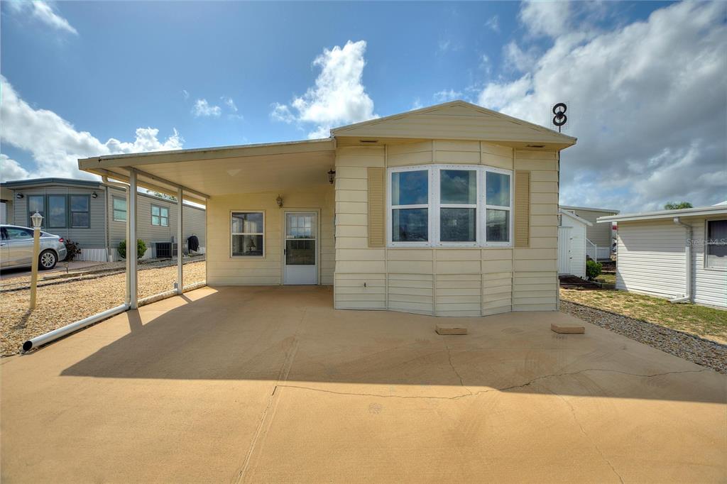 A beige manufactured home features a covered carport and a bay window under a blue sky — 251 PATTERSON ROAD UNIT G9, HAINES CITY, FL