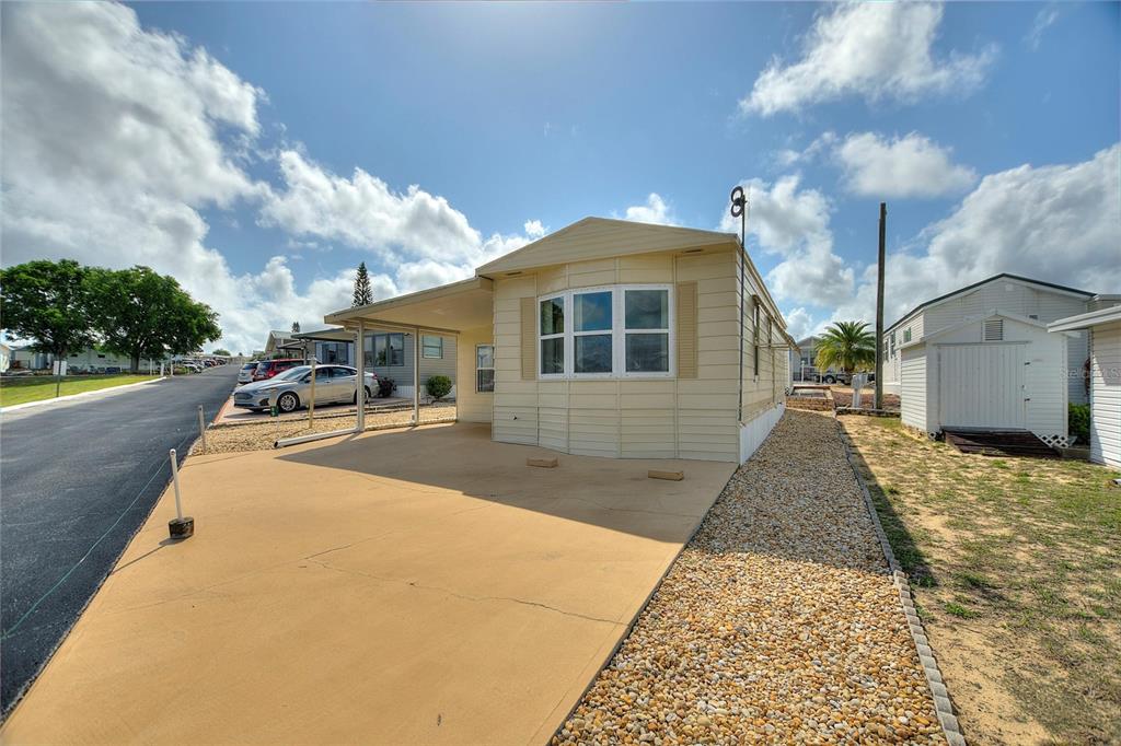 A light-colored mobile home features a concrete carport, a bay window, and a gravel yard — 251 PATTERSON ROAD UNIT G9, HAINES CITY, FL