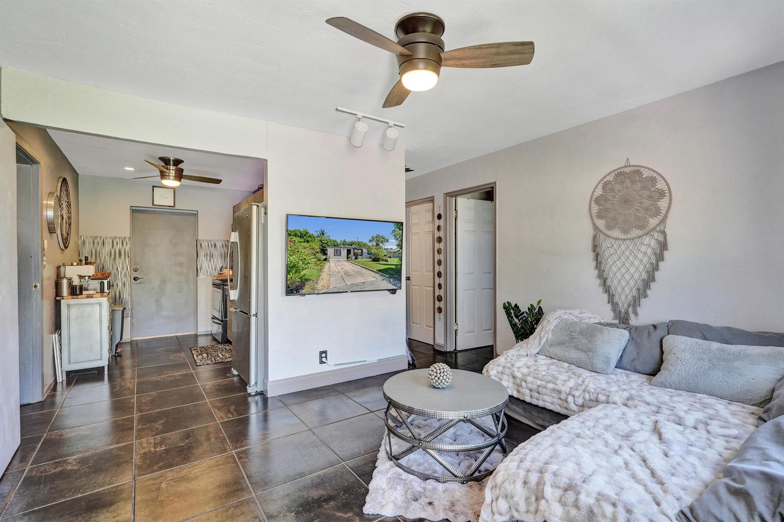 A living room features dark tile floors, a ceiling fan, a wall-mounted television, and furniture — 1465 NE 27th Street, Pompano Beach FL 33064, POMPANO BEACH, FL