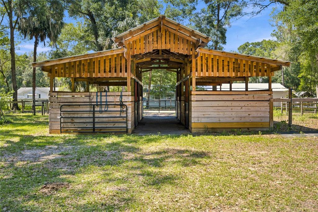 A wooden horse barn with a center aisle stands in a grassy, tree-filled yard — 14000 NE 47TH AVENUE, ANTHONY, FL