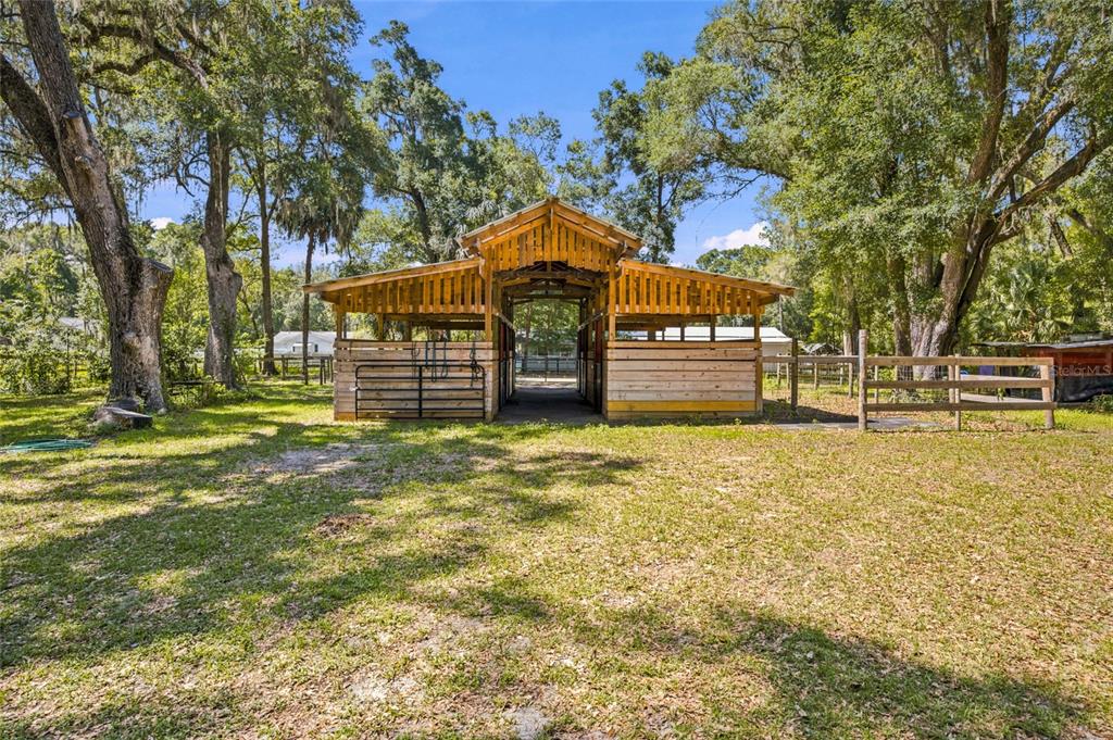 A wooden horse barn stands in a grassy, tree-filled yard under a blue sky — 14000 NE 47TH AVENUE, ANTHONY, FL