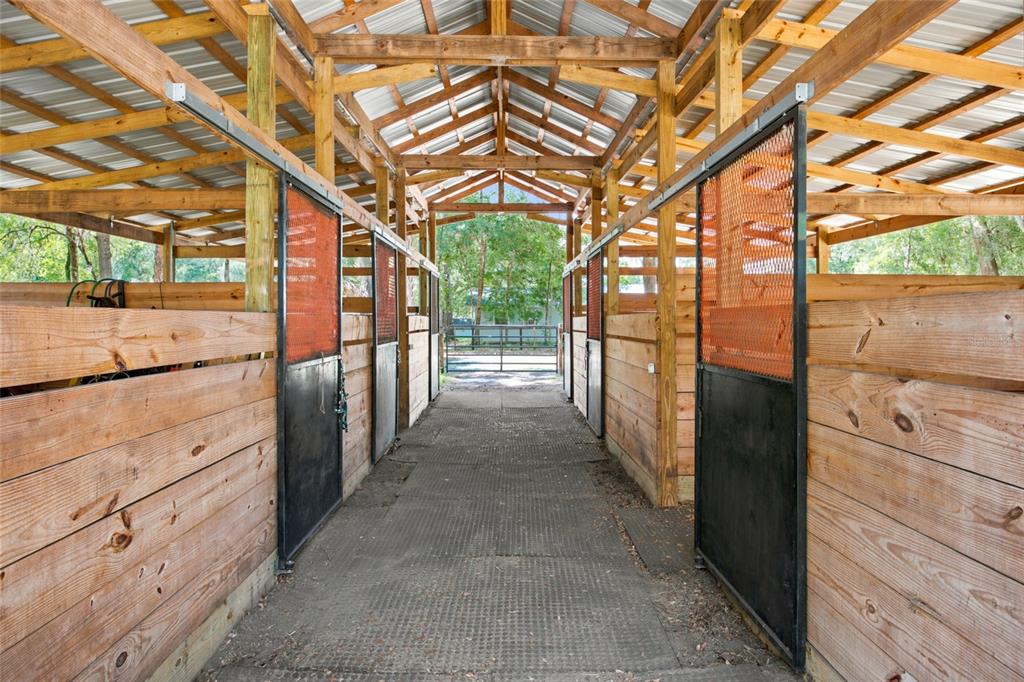 A central aisle leads through a wooden horse stable with metal mesh stall doors — 14000 NE 47TH AVENUE, ANTHONY, FL