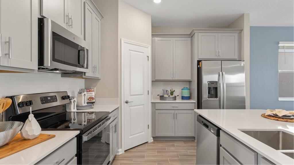 A modern kitchen features gray cabinets, stainless steel appliances, and a white quartz island countertop — 5658 KETTLEBELL ALLEY, CLERMONT, FL