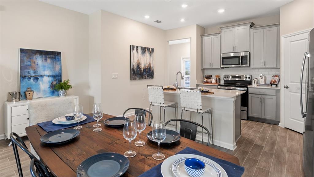A dining area with a wooden table leads into a kitchen with gray cabinets — 5658 KETTLEBELL ALLEY, CLERMONT, FL