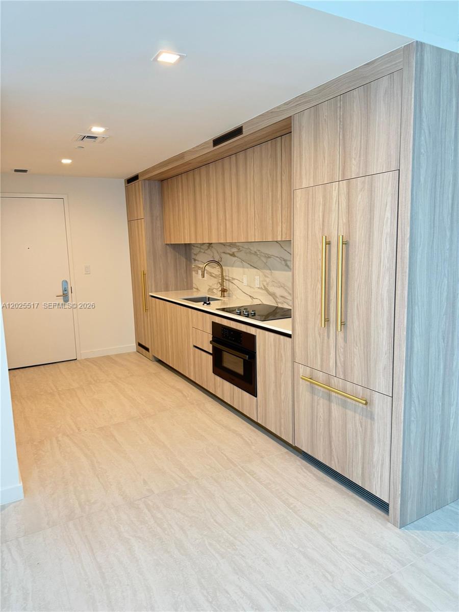 A modern kitchen features light wood cabinetry, gold hardware, and a marble-patterned backsplash — 77 SE 5 # 2307, Miami FL 33131, MIAMI, FL