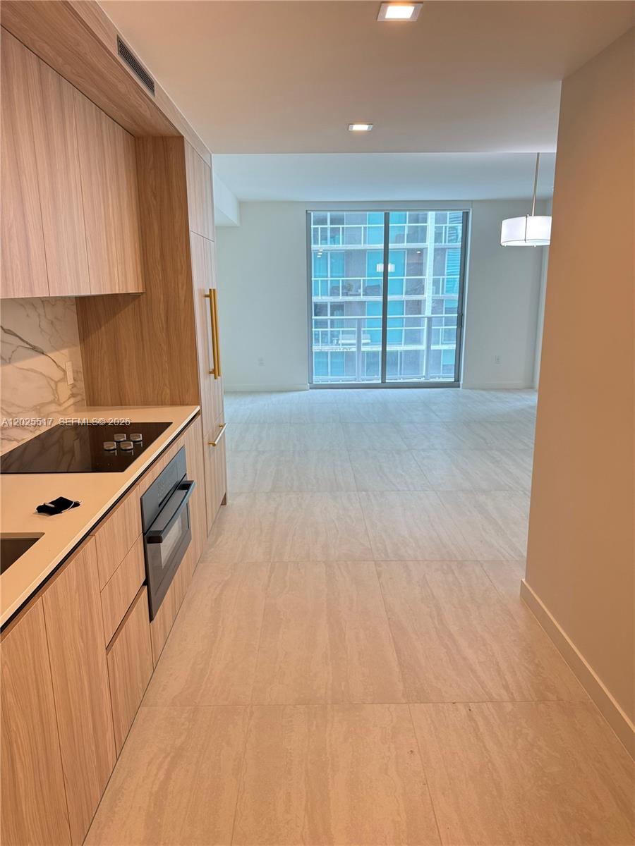 A modern kitchen with light wood cabinetry and stainless steel appliances opens to a living area — 77 SE 5 # 2307, Miami FL 33131, MIAMI, FL