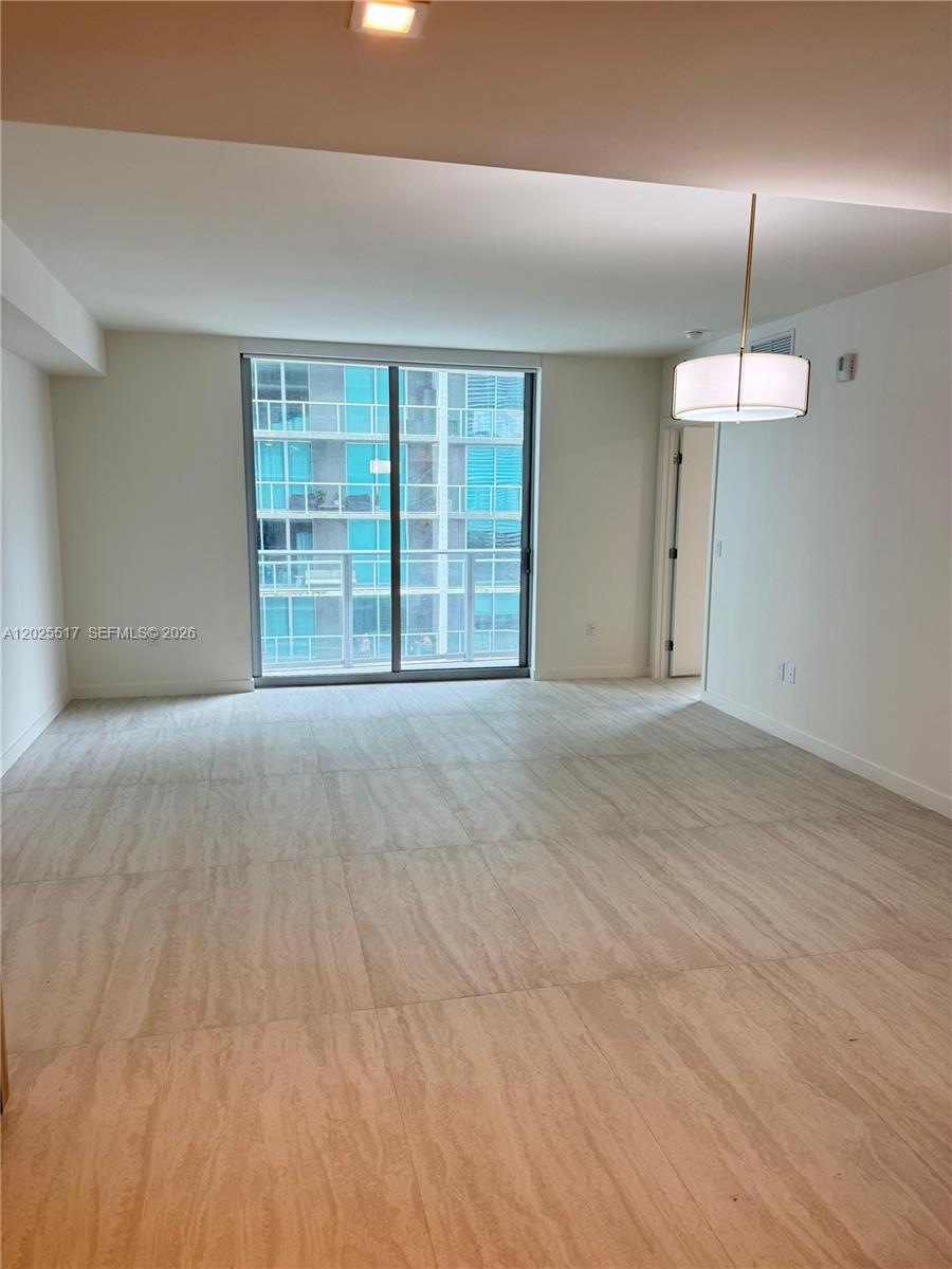An empty room features light-colored tile flooring, a modern pendant light, and a sliding glass door — 77 SE 5 # 2307, Miami FL 33131, MIAMI, FL