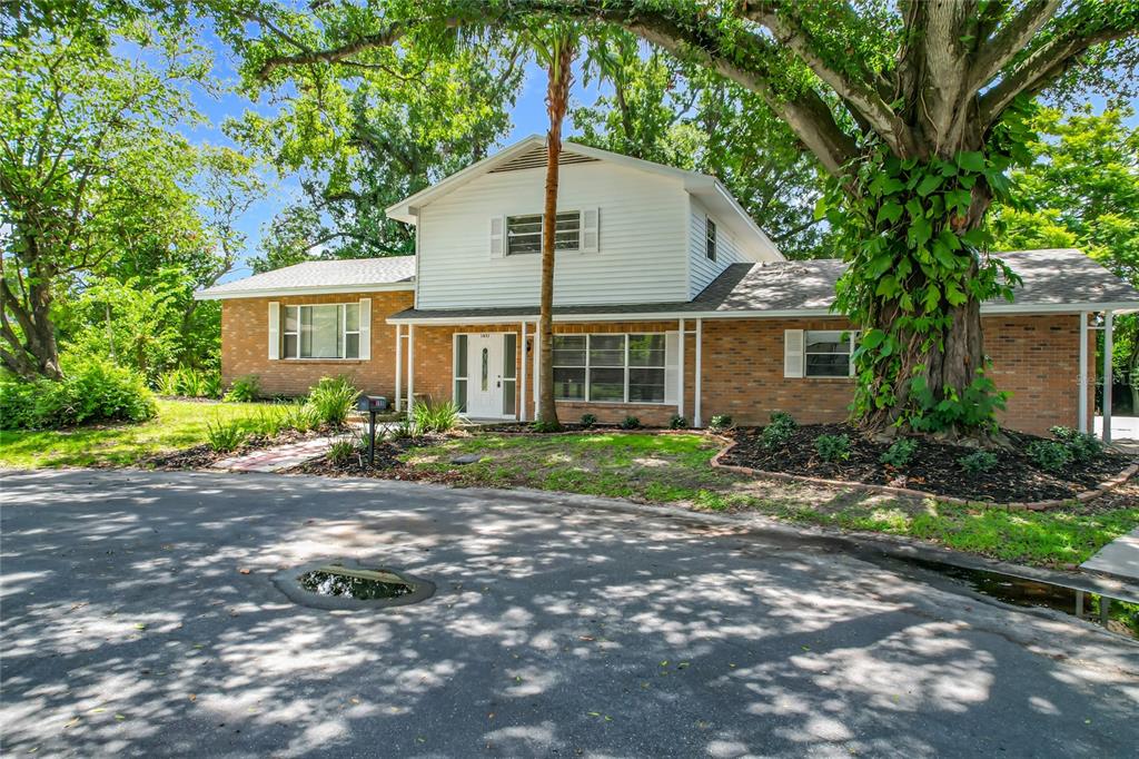 A two-story house with a brick and white siding exterior sits behind a large tree — 1631 MONTEREY LANE, LAKELAND, FL