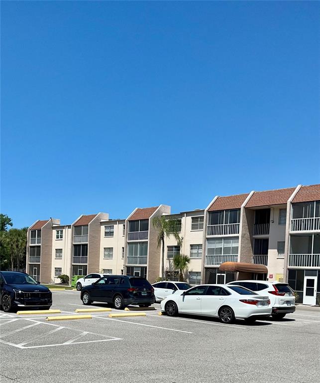 A multi-story apartment building with balconies stands behind a parking lot with several cars — 519 ALBEE FARM ROAD UNIT 303, VENICE, FL