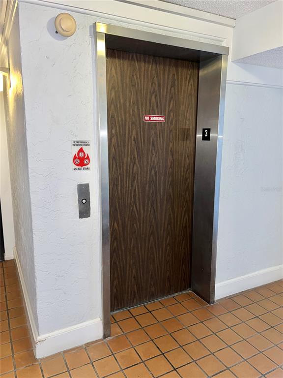 An elevator with a wood-grain door is located in a tiled hallway — 519 ALBEE FARM ROAD UNIT 303, VENICE, FL