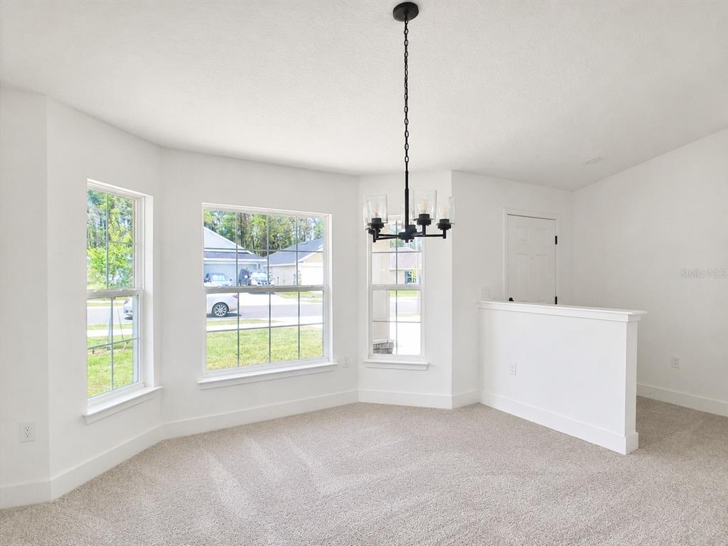 A dining area with carpeted floors, a black chandelier, and large windows overlooking a neighborhood — 262 VERNY GROVE LANE, LEESBURG, FL