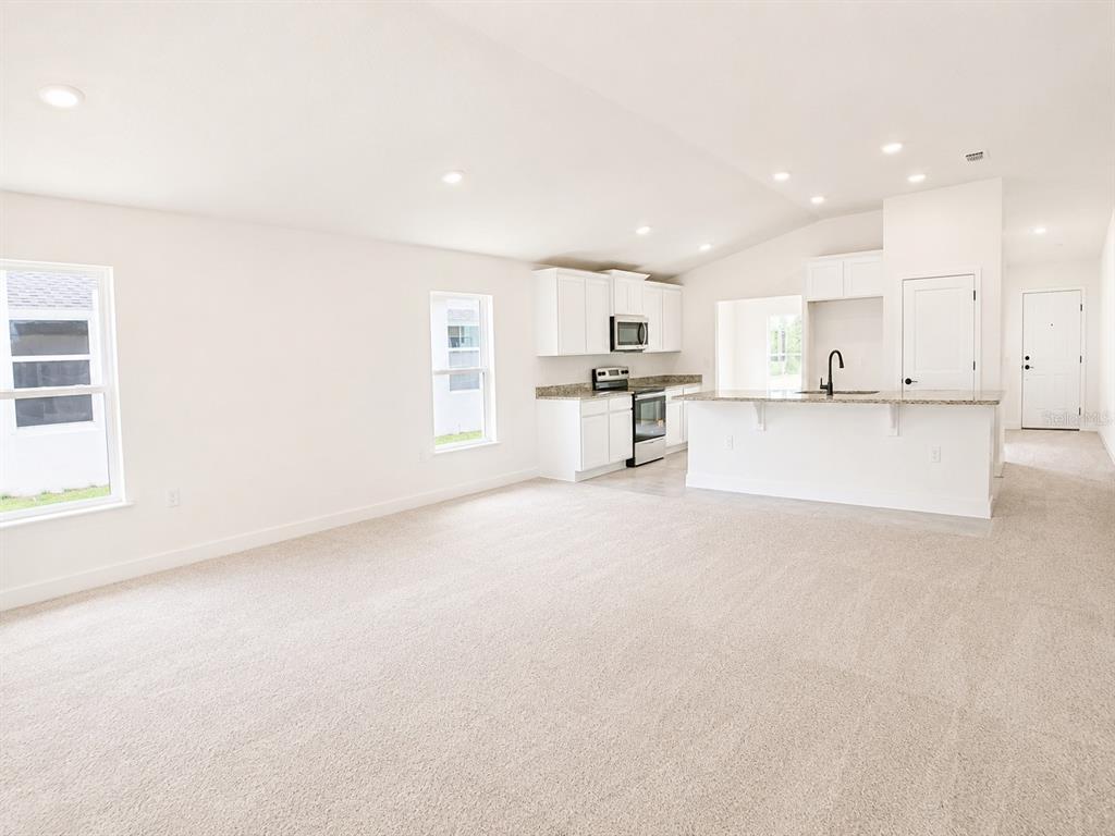 A bright, open-concept living room features neutral carpeting, white walls, and an adjacent kitchen — 262 VERNY GROVE LANE, LEESBURG, FL