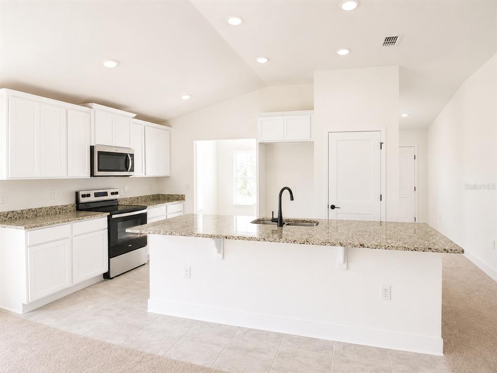 A kitchen features white cabinets, granite countertops, a center island with a sink, and appliances — 262 VERNY GROVE LANE, LEESBURG, FL