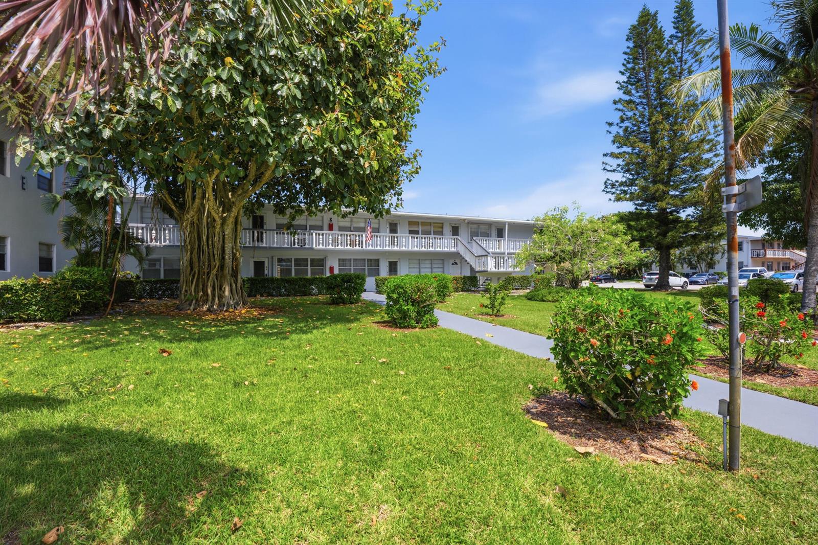 A two-story apartment building with a white balcony sits behind a large tree and lawn — 98 E Cambridge E, West Palm Beach FL 33417, WEST PALM BEACH, FL