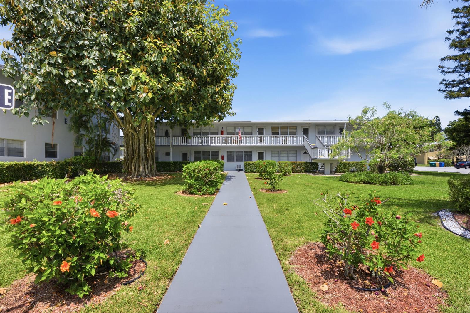 A gray walkway leads to a two-story apartment building with a large tree and landscaping — 98 E Cambridge E, West Palm Beach FL 33417, WEST PALM BEACH, FL