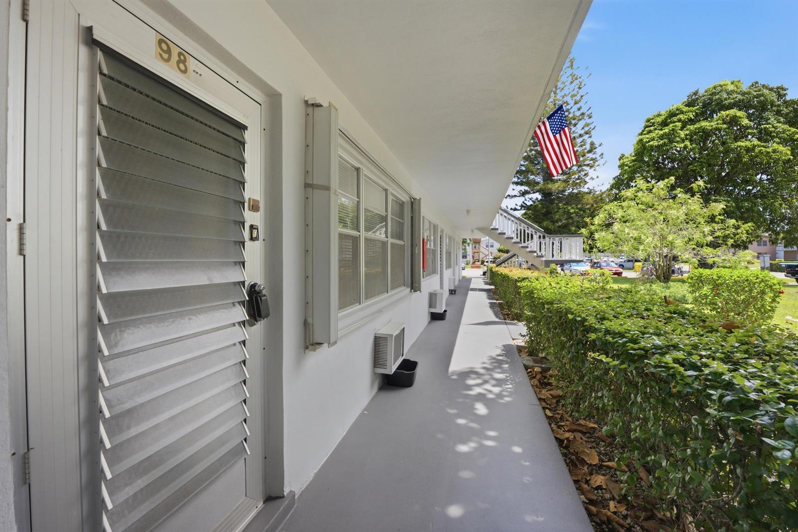 An exterior walkway leads past apartment doors with louvered shutters and wall-mounted air conditioning units — 98 E Cambridge E, West Palm Beach FL 33417, WEST PALM BEACH, FL