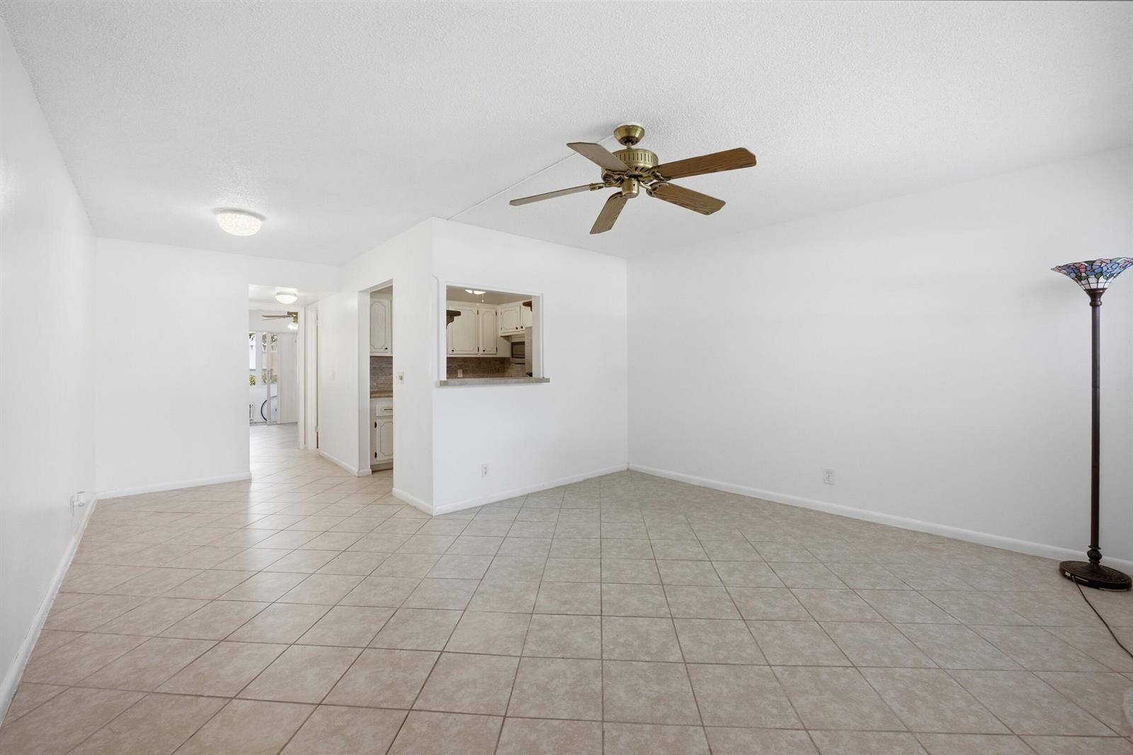 A bright, empty living room features beige tile flooring, white walls, and a ceiling fan — 98 E Cambridge E, West Palm Beach FL 33417, WEST PALM BEACH, FL