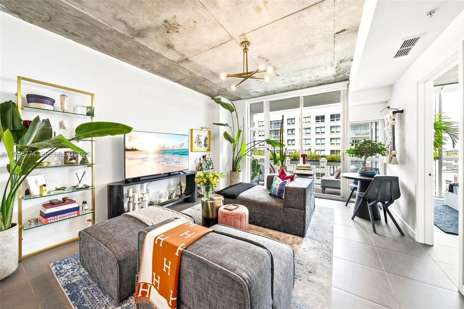 A modern living room features a concrete ceiling, gray modular seating, and a balcony view — 3301 NE 1st Ave # H0805, Miami FL 33137, MIAMI, FL