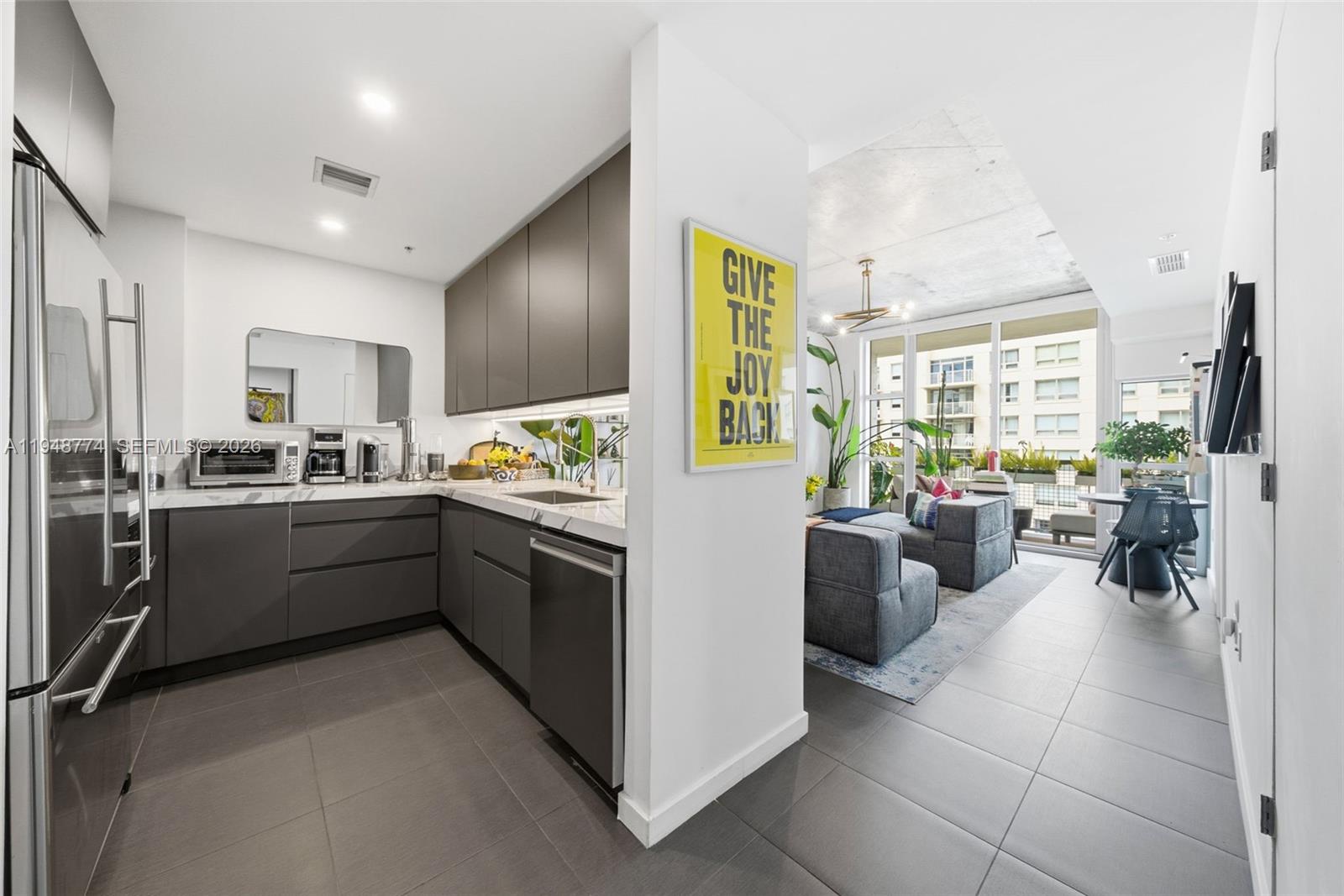 A modern kitchen with dark grey cabinetry and tile flooring opens into a living area — 3301 NE 1st Ave # H0805, Miami FL 33137, MIAMI, FL