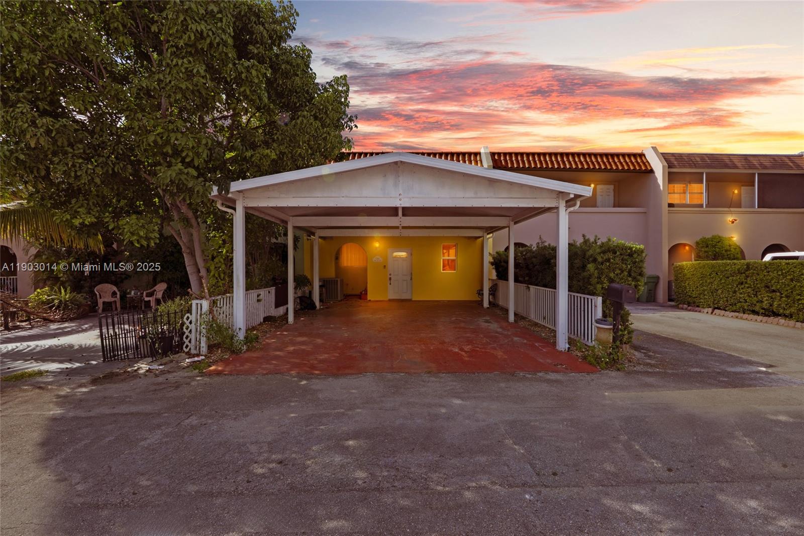 A yellow house features a white carport and a paved driveway under a sunset sky — 7144 W 2nd Ln, Hialeah FL 33014, HIALEAH, FL