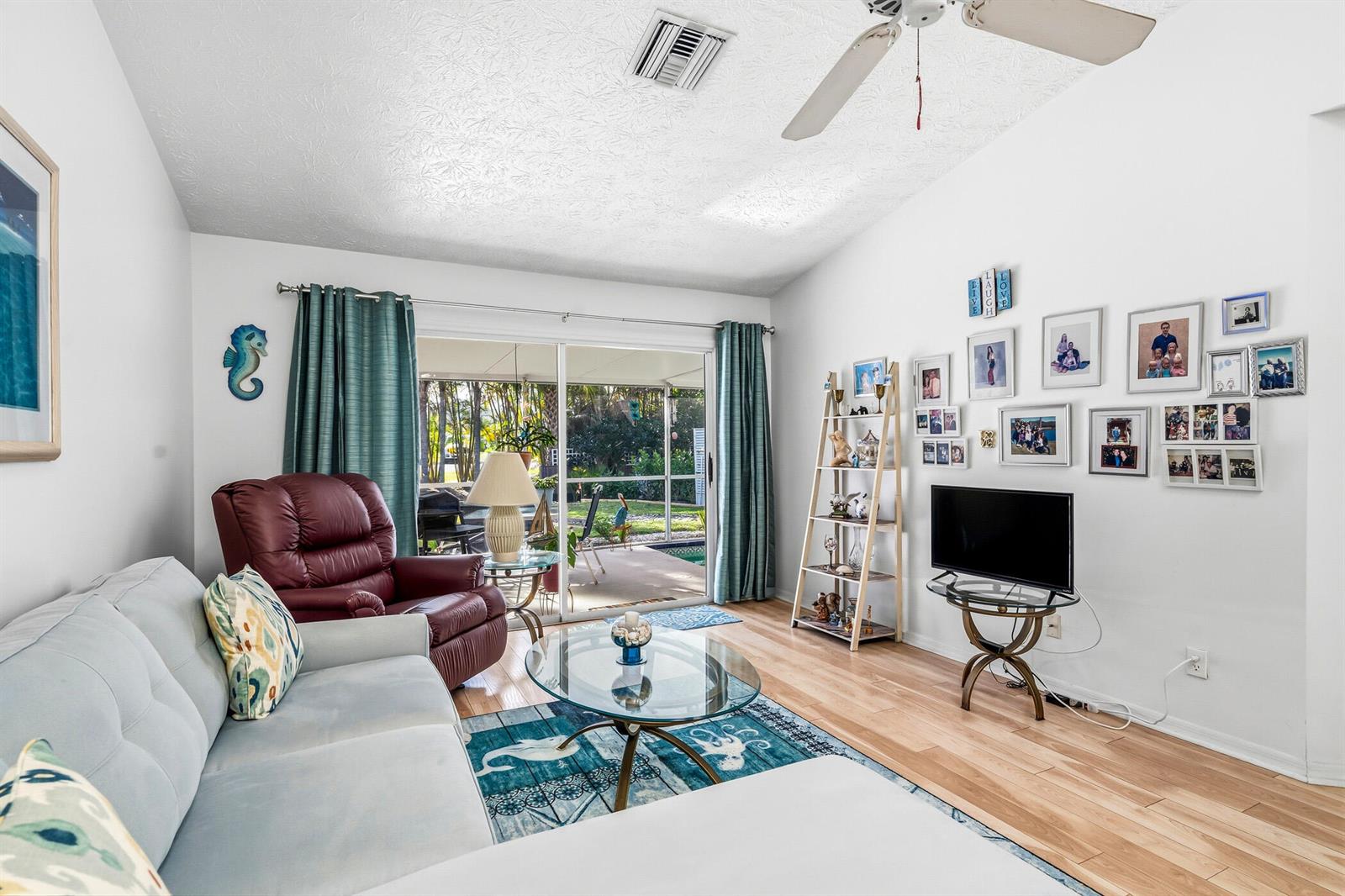 A living room features a light-colored sofa, a red recliner, and a glass-topped coffee table — 1866 Sixty Oaks Lane, Vero Beach FL 32966, VERO BEACH, FL
