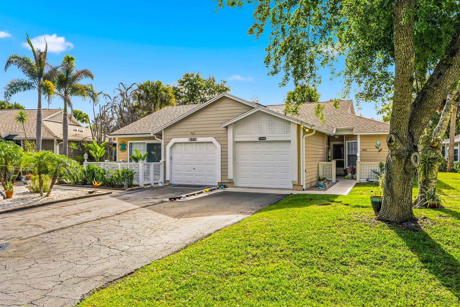 A tan duplex with two white garage doors and a shared driveway under a blue sky — 1866 Sixty Oaks Lane, Vero Beach FL 32966, VERO BEACH, FL
