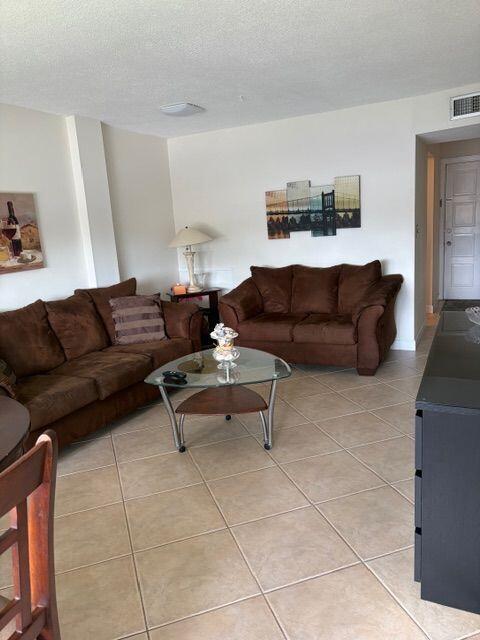 A living room features brown sofas, a glass coffee table, and tile flooring — 2562 Garden Drive N # 305, FL 33461, FL