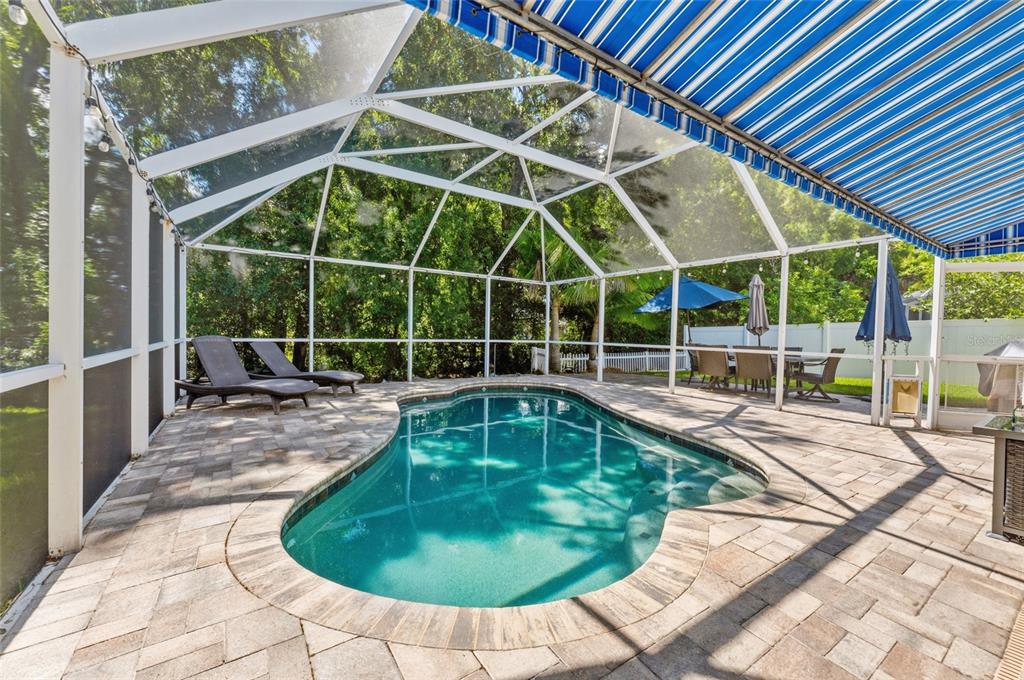 A screened-in pool area features a kidney-shaped pool, stone pavers, and a blue striped awning — 15629 EASTBOURN DRIVE, ODESSA, FL