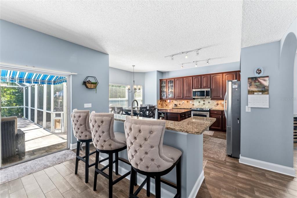 A kitchen with dark wood cabinets, granite countertops, and three tufted bar stools — 15629 EASTBOURN DRIVE, ODESSA, FL