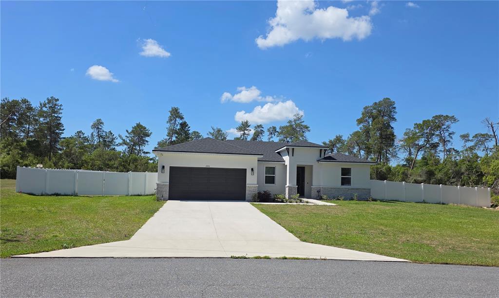 A single-story house with a white exterior, stone accents, and a dark garage door — 2450 SW 170TH LOOP, OCALA, FL