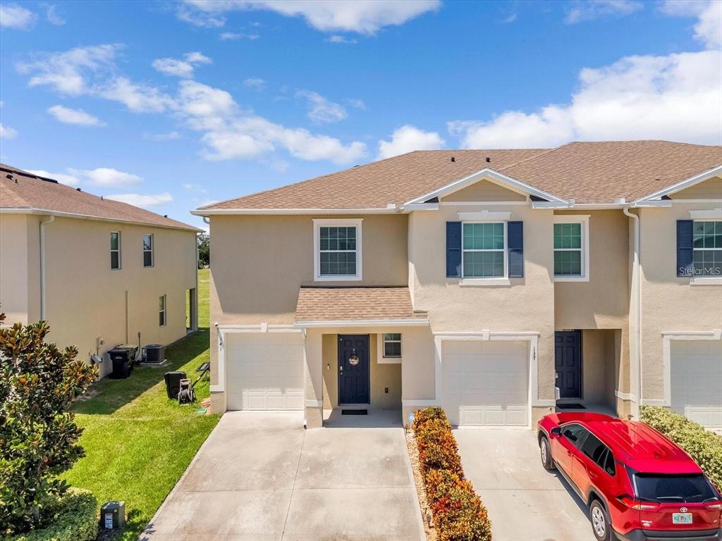 A two-story tan townhouse with a white garage and a red SUV parked in front — 141 FELTRIM RESERVE BOULEVARD, DAVENPORT, FL