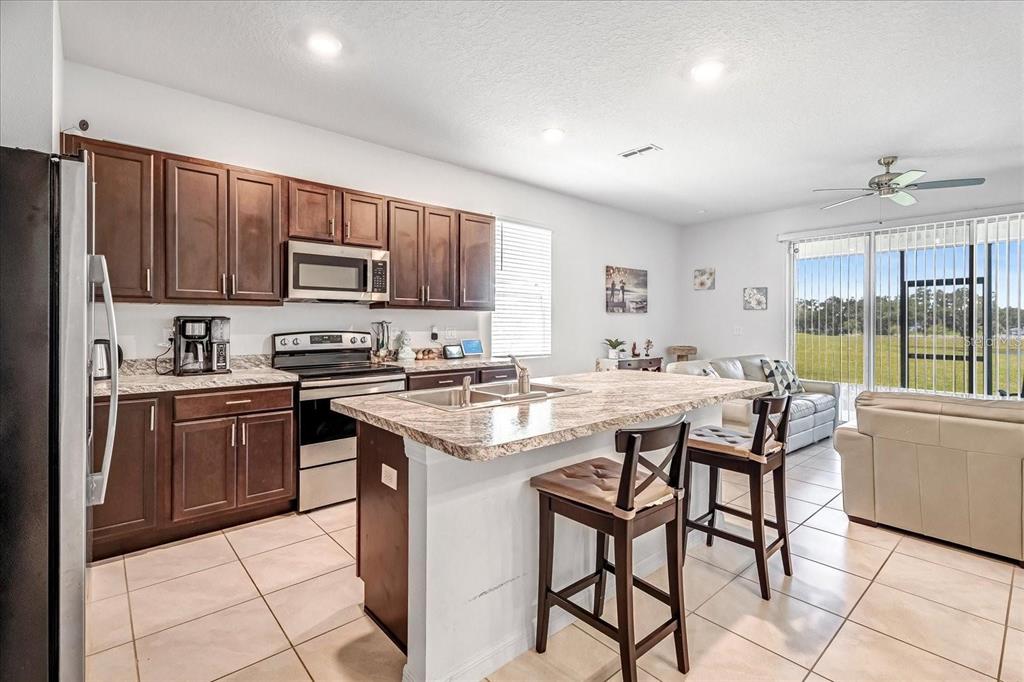 A kitchen with dark wood cabinets, granite countertops, and a central island with bar stools — 141 FELTRIM RESERVE BOULEVARD, DAVENPORT, FL