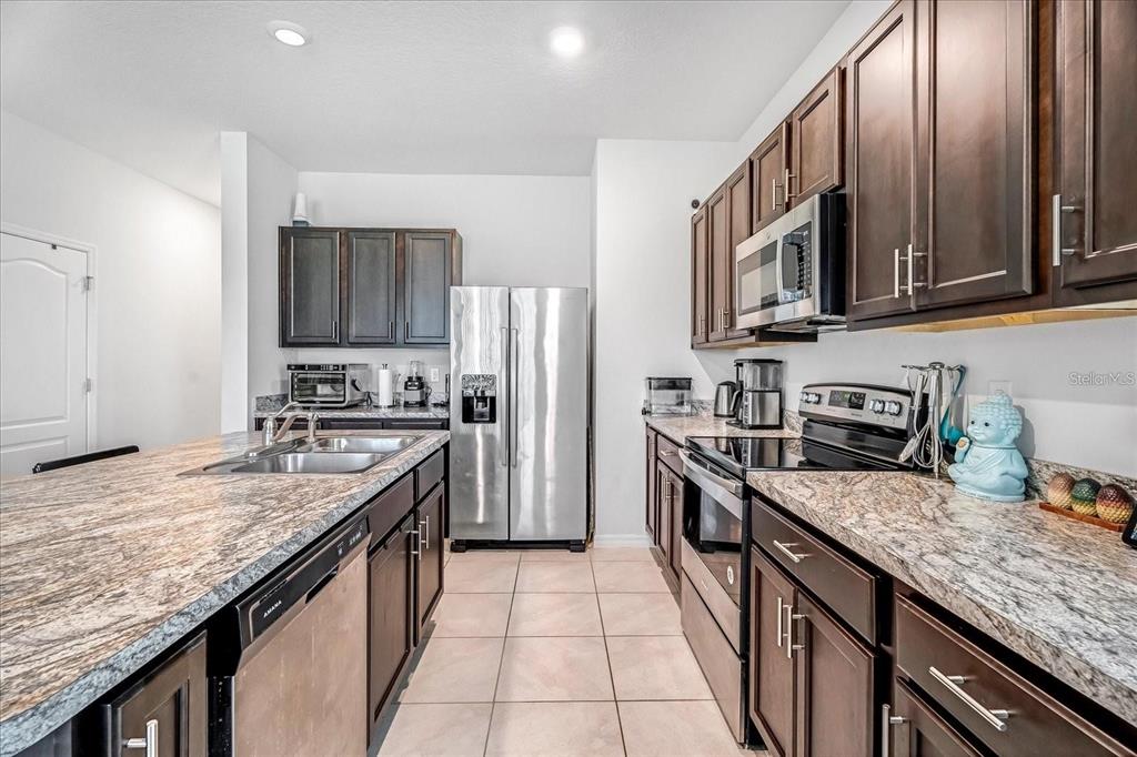 A kitchen features dark wood cabinets, granite countertops, stainless steel appliances, and tile flooring — 141 FELTRIM RESERVE BOULEVARD, DAVENPORT, FL
