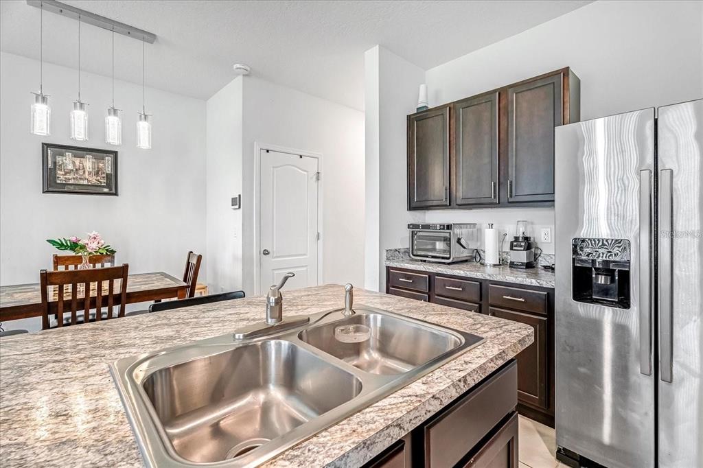 A kitchen features a granite-topped island with a double sink, dark cabinetry, and stainless appliances — 141 FELTRIM RESERVE BOULEVARD, DAVENPORT, FL