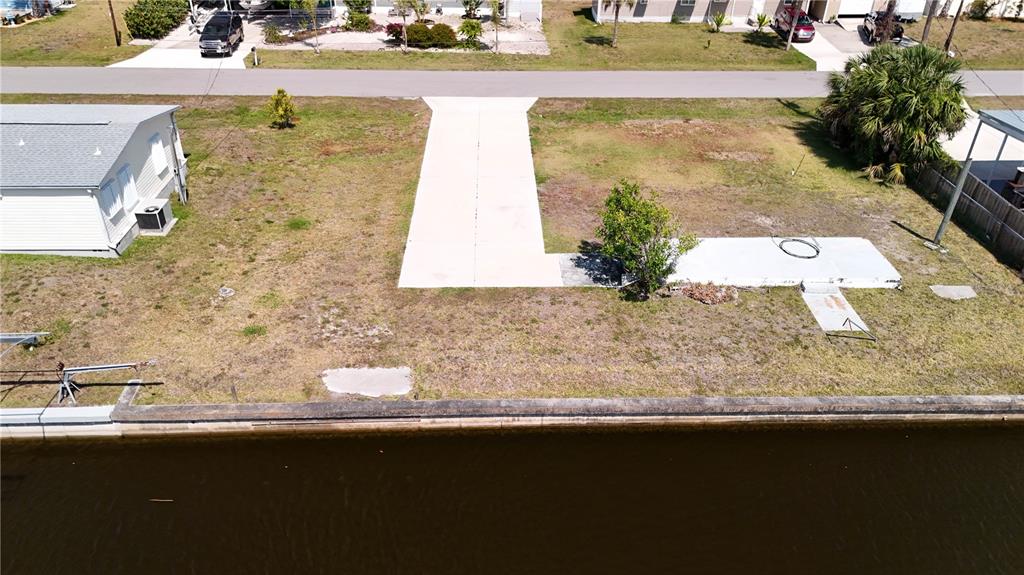 An aerial view shows a vacant waterfront lot with a concrete driveway and seawall — 4239 WOOD DUCK ROAD, PORT CHARLOTTE, FL