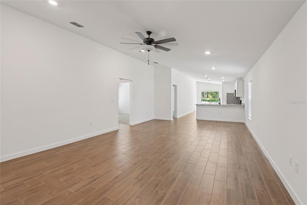 An open-concept living area features white walls, wood-look tile flooring, and a kitchen in back — 13331 CANADA GOOSE ROAD, WEEKI WACHEE, FL