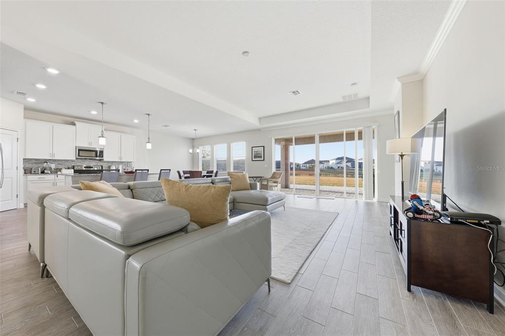 A spacious open-concept living room features a grey sectional sofa, tile flooring, and sliding glass doors — 4524 SEQUEL ROAD, KISSIMMEE, FL