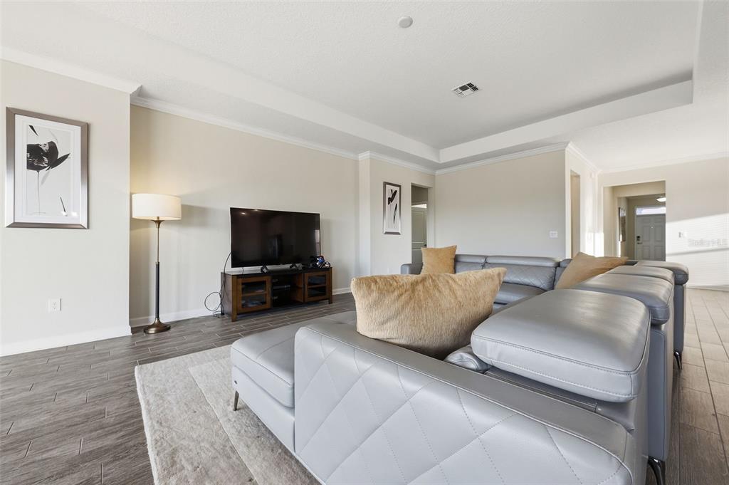 A living room features a grey sectional sofa, a television on a stand, and wood-look flooring — 4524 SEQUEL ROAD, KISSIMMEE, FL