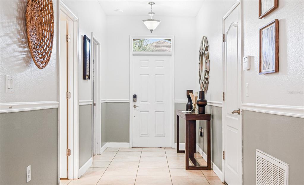 A bright entryway features white walls with gray wainscoting, tile flooring, and a wooden console table — 9026 SHADOW MOUNTAIN STREET, DAVENPORT, FL