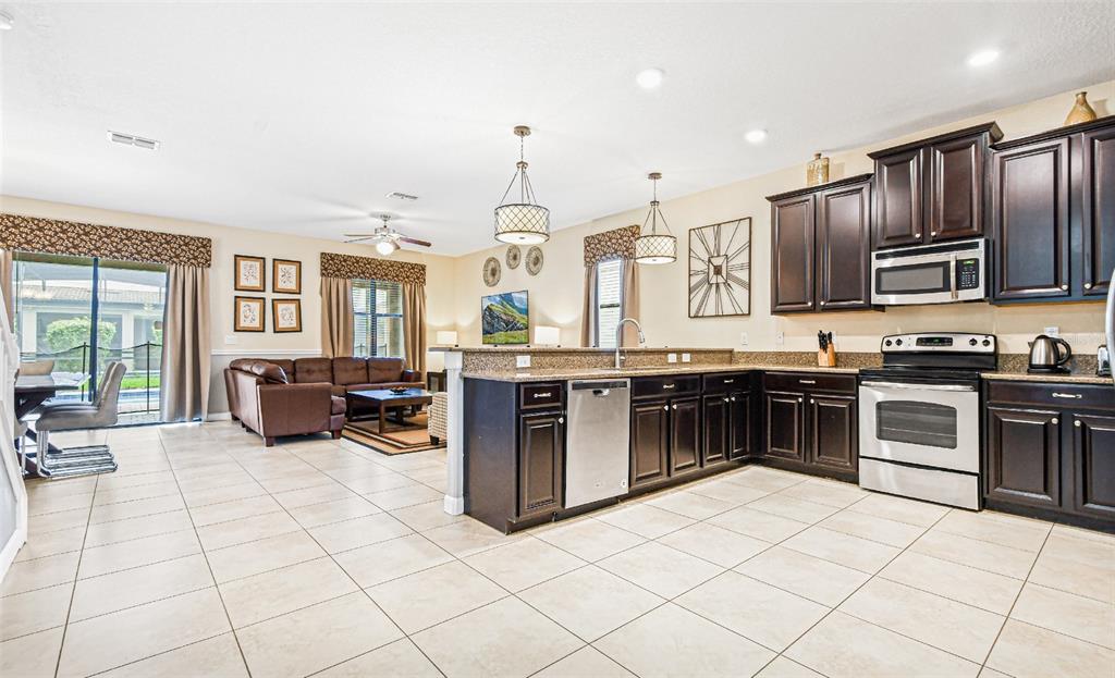 A kitchen with dark wood cabinets and stainless steel appliances opens to a living area — 9026 SHADOW MOUNTAIN STREET, DAVENPORT, FL