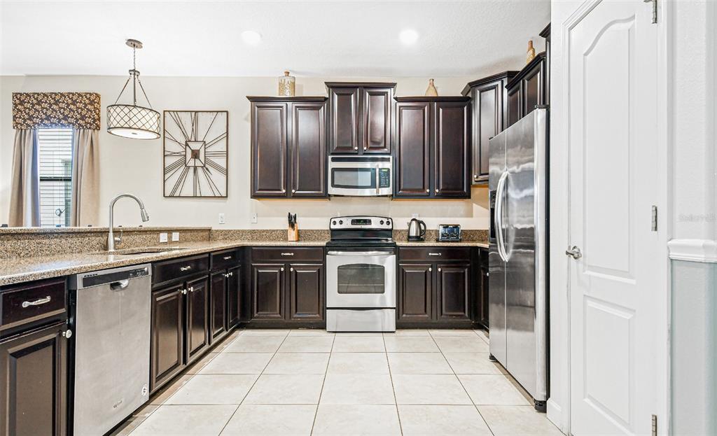 A kitchen features dark wood cabinets, stainless steel appliances, granite countertops, and light tile flooring — 9026 SHADOW MOUNTAIN STREET, DAVENPORT, FL