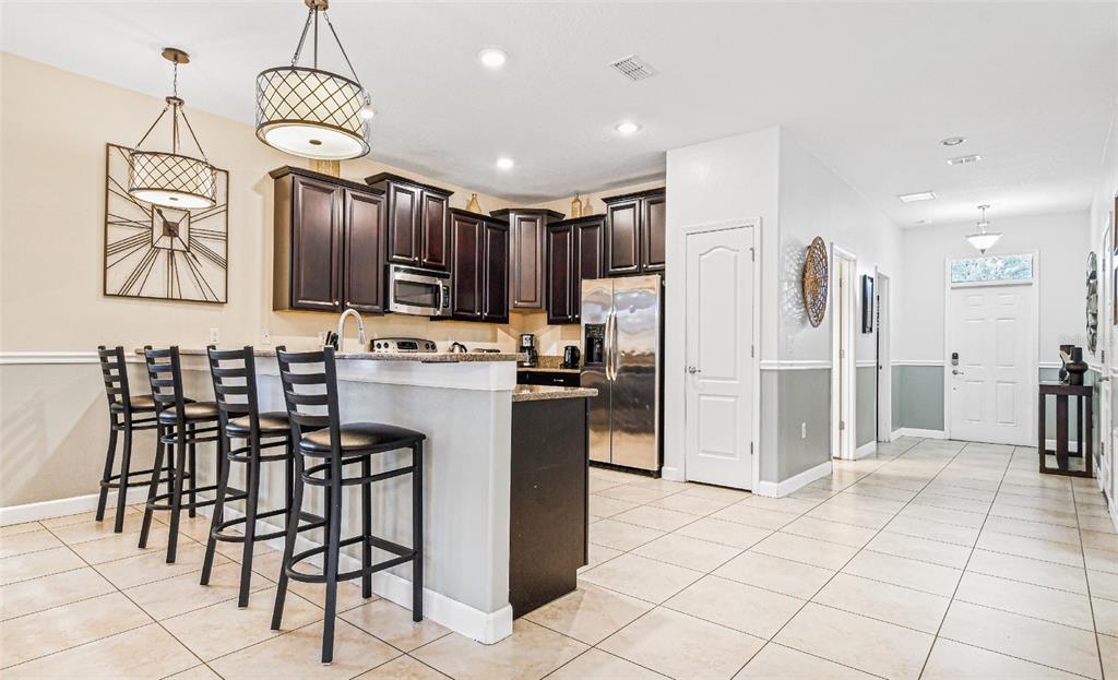 A kitchen with dark wood cabinets, granite countertops, and a breakfast bar with four stools — 9026 SHADOW MOUNTAIN STREET, DAVENPORT, FL