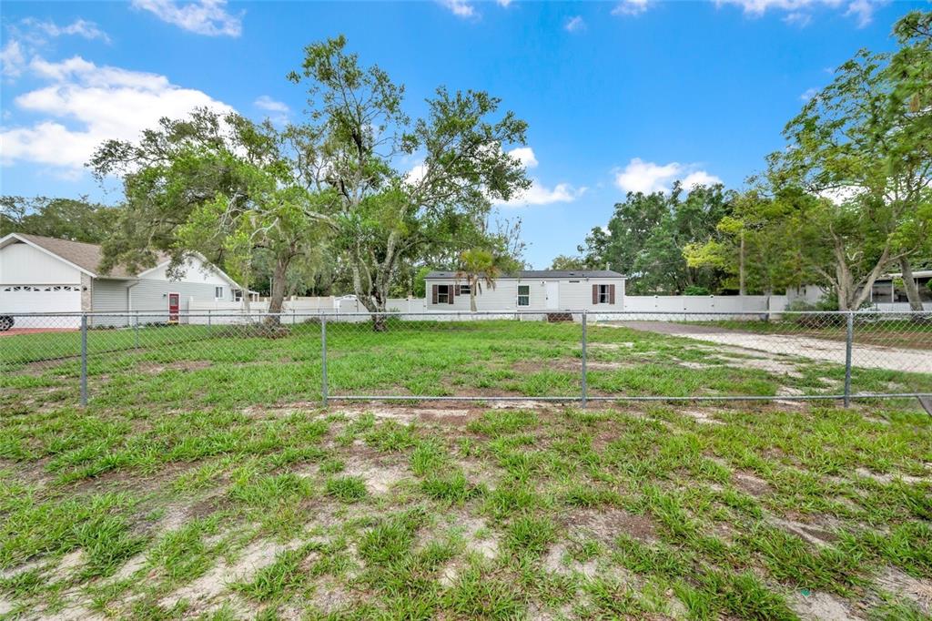 A fenced grassy yard leads to a single-story house with a driveway and mature trees — 7194 SEALAWN DRIVE, SPRING HILL, FL