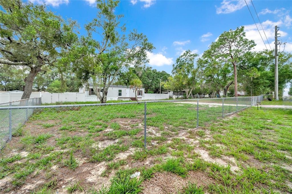 A fenced, grassy lot with scattered trees sits in front of a single-story house — 7194 SEALAWN DRIVE, SPRING HILL, FL