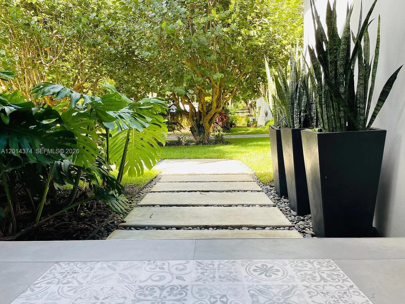 A stone walkway leads through a garden past tall planters toward a grassy yard — 336 NE 85, El Portal FL 33138, EL PORTAL, FL