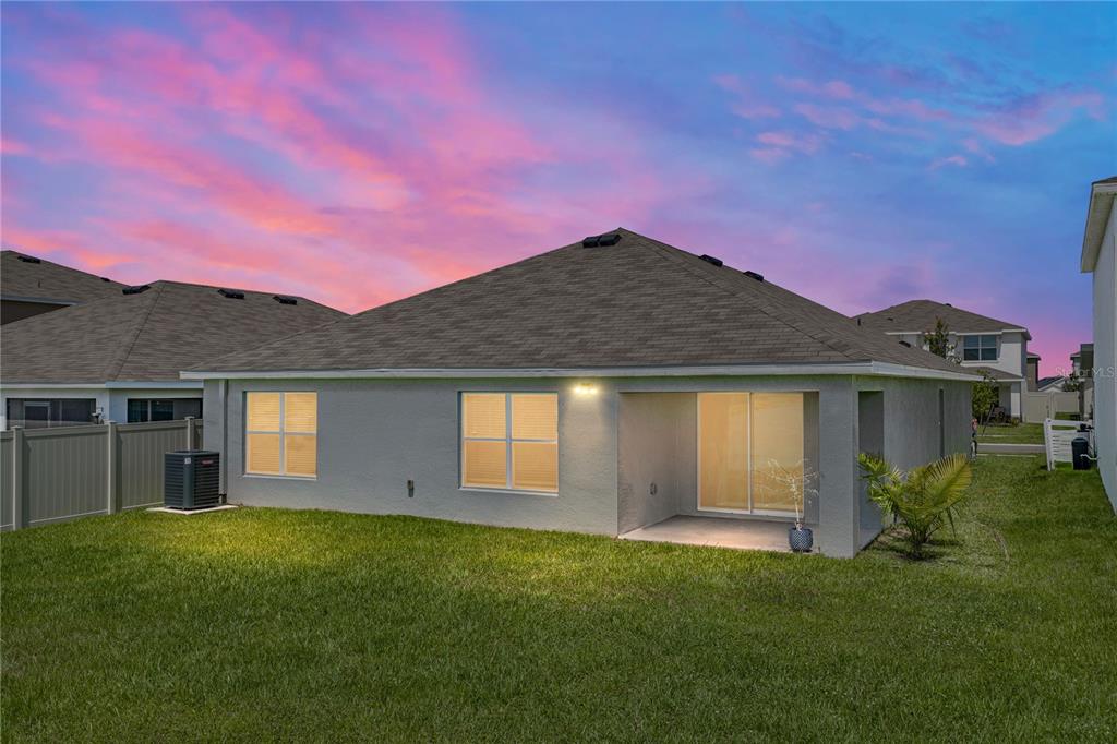 The rear exterior of a single-story house features a covered patio, lawn, and vinyl fencing — 3062 LIVING CORAL STREET, WIMAUMA, FL