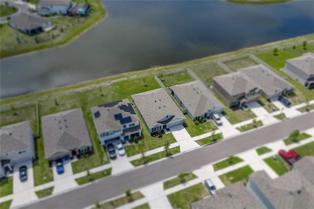 An aerial view shows a suburban neighborhood with houses along a lake — 3062 LIVING CORAL STREET, WIMAUMA, FL