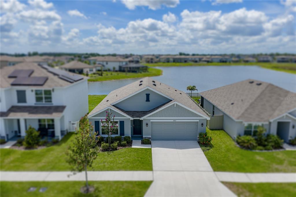 An aerial view shows a single-story suburban house with a gray garage and lakefront backyard — 3062 LIVING CORAL STREET, WIMAUMA, FL