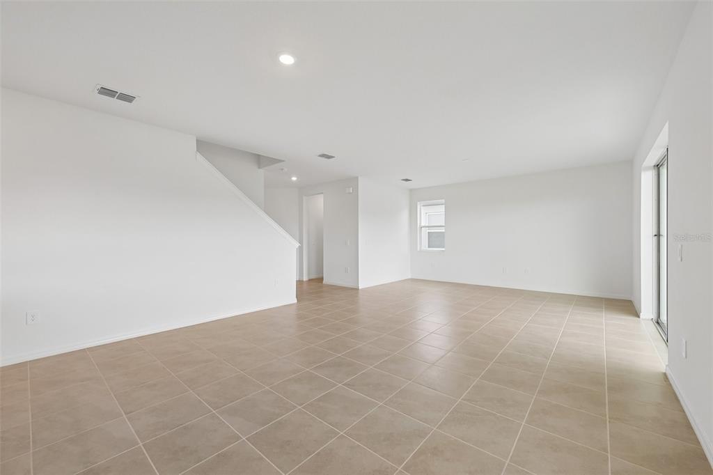 An open-concept living area features white walls, tan tile flooring, and a staircase — 4508 OUTHAUL RUN, PALMETTO, FL